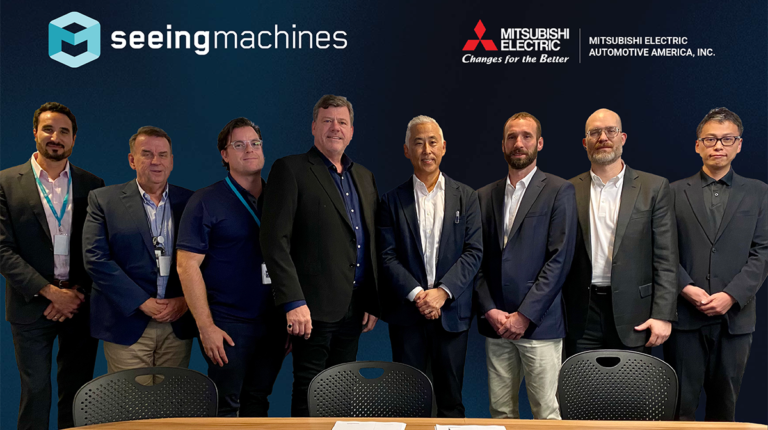 Seeing Machines and Mitsubishi Electric Automotive America joined forces through a referral agreement. Senior staff from both companies are pictured here lined up behind a wooden desk with the signed agreement on the table in front of them.