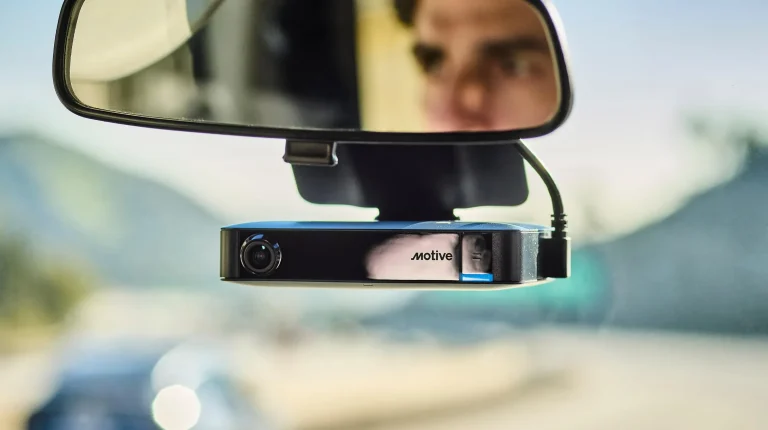 Motive's AI Dashcam Plus hangs below the rearview mirror. The driver's face can be seen in the mirror