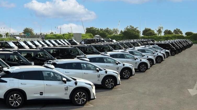 WeRide and Uber's Robotaxi fleet parked in a group in Abu Dhabi. The vehicles are white cars and larger black vans and minibuses.