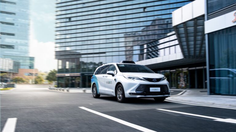 A Pony-Ai robotaxi drives along a sleep urban road with glass-fronted buildings in the background.