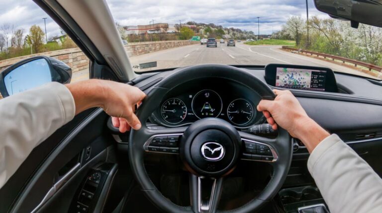 Study finds Mazda ADAS bundles deliver compounding crash claim benefits View from the driver's seat of a car on a quiet highway, with the driver's hands on the steering wheel.