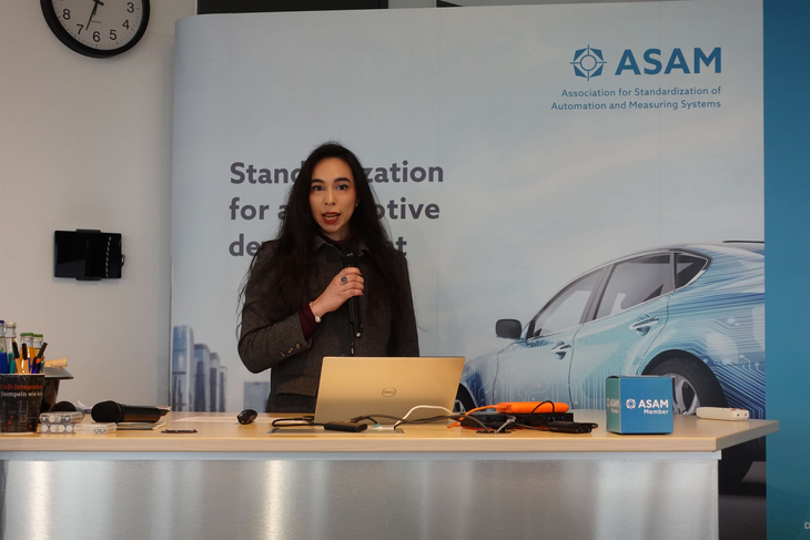 UKi brand manager – automotive, Charlotte Iggulden gives a presentation at ASAM's 2026 Technical Seminar. She is wearing a black suit and holding a microphone.