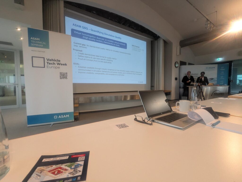 Yash and Ahmed's presentation on simulation quality at at ASAM’s Technical Seminar 2026. They are standing at a lectern in front of a large projector screen in front of rows of attendees.