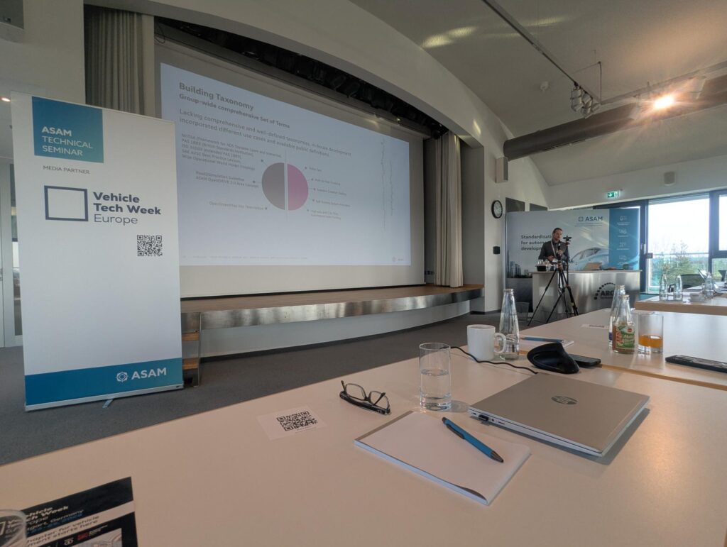 Andreas Richter, engineering program manager at Volkswagen, gives a presentation at ASAM’s Technical Seminar 2026. He is standing at a lectern in front of a large projector screen in front of rows of attendees. 