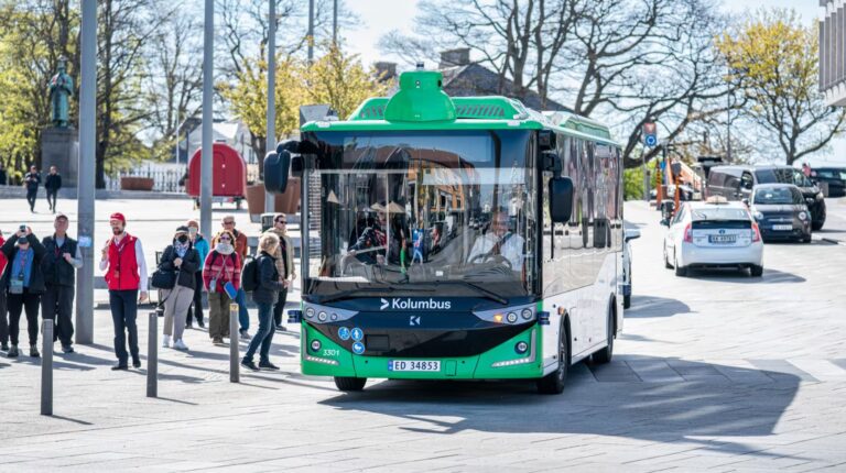 The Karsan autonomous e-ATAK autonomous bus, with a green and white exterior, picks up passengers along a transit route.
