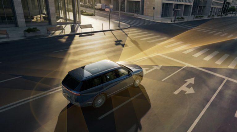 An autonomous vehicle approaches a four-way intersection. Yellow lights illustrate its connectivity.