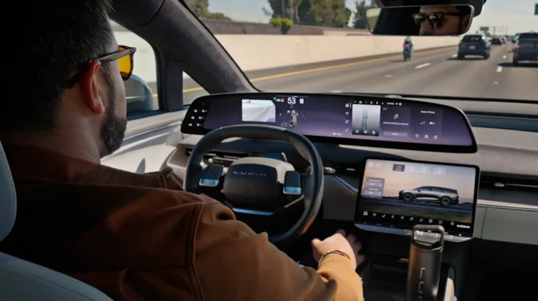 Hands-free driving and smarter navigation added to Lucid Gravity Interior view of the driver's position in the Luci Gravity, with a wide touchscreen display, steering wheel and a quiet highway scene visible through the windshield.