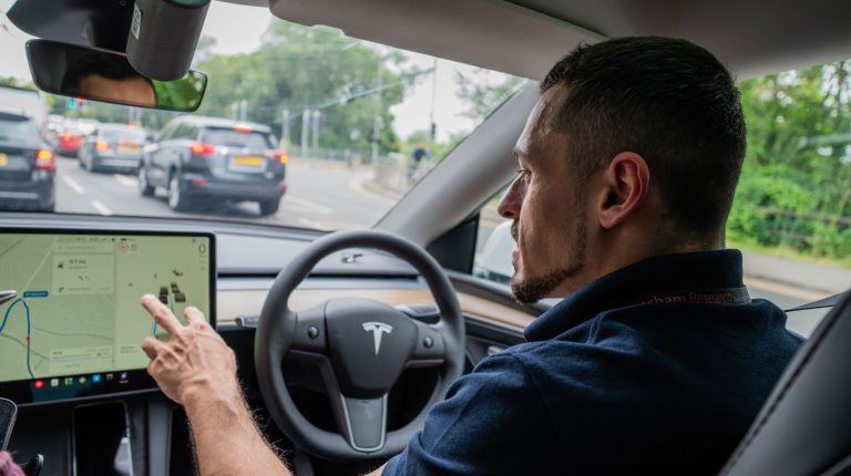 Thatcham Research ISA testing carried out in a car, with a testing operative in the driver's seat with their hands on the steering wheel and a touchscreen.