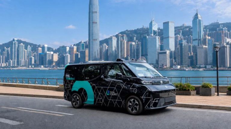 WeRide and Geely Farizon launch right-hand-drive robotaxi in Hong Kong A black WeRide autonomous Robotaxi drives along a waterside road in Hong Kong, with skyscrapers in the background.