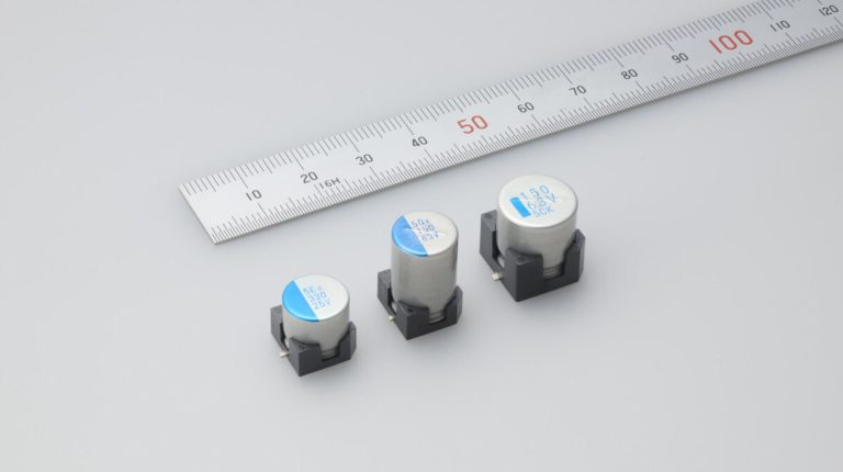 Taiyo Yuden commercializes hybrid aluminum electrolytic capacitors The Taiyo Yuden HVX (-K) and HTX (-K) hybrid aluminum electrolytic capacitors shown on a white table in front of a ruler to demonstrate their size.
