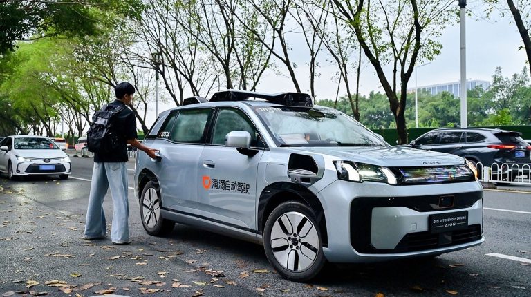 DiDi’s next-gen R2 robotaxi begins driverless trials in China A passenger opens the read door to a grey DiDi Autonomous Driving Robotaxi R2 vehicle in an urban environment.